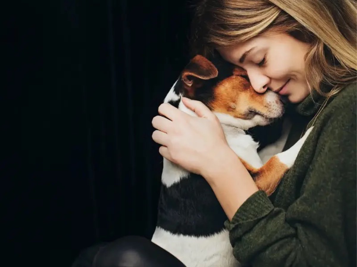 Frau umarmt vertrauensvoll ihren Hund mit geschlossenen Augen, sichtbares Vertrauen zwischen Mensch und Hund